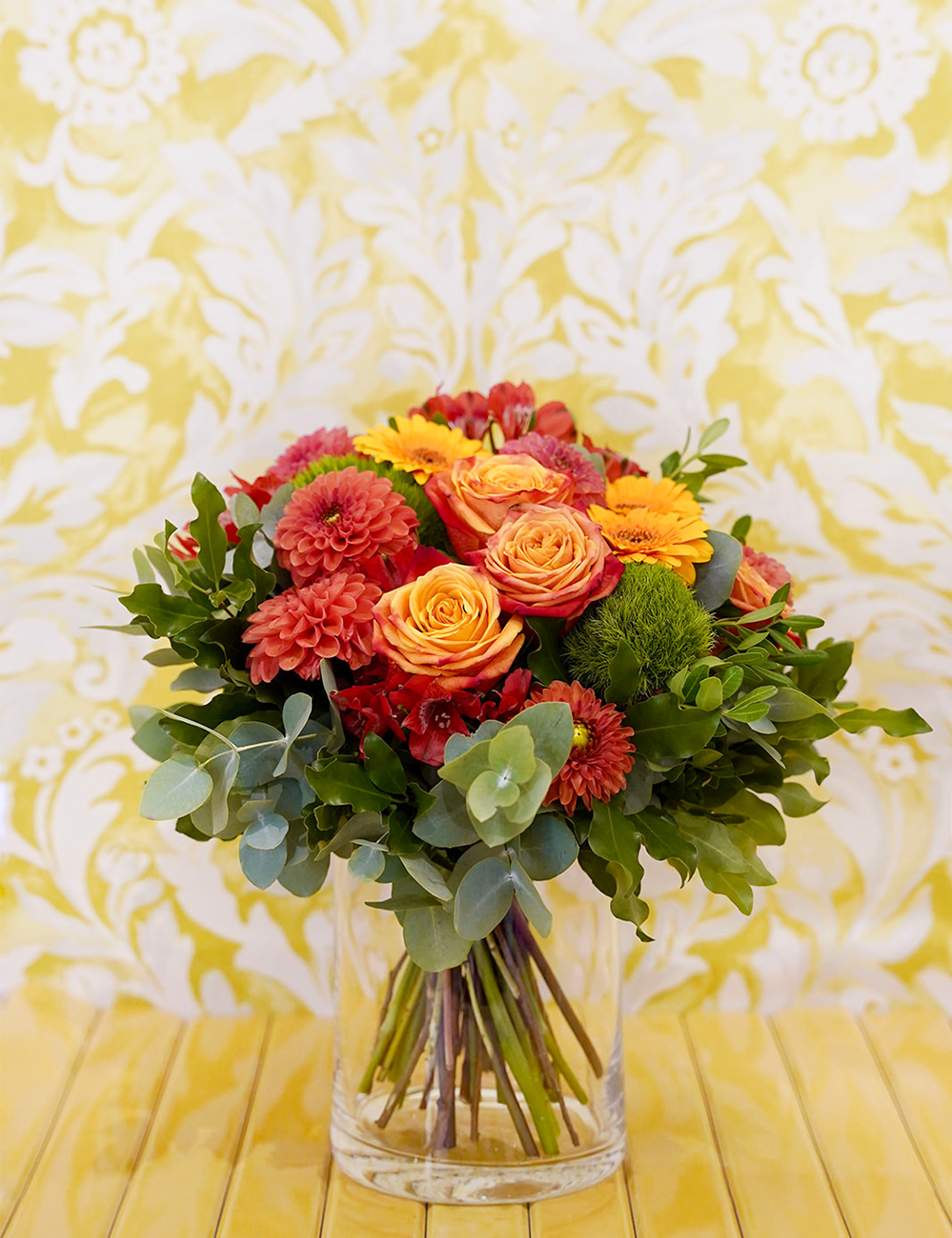 Bouquet de fleurs rond dans les tons rouges et oranges avec des touches de vert.