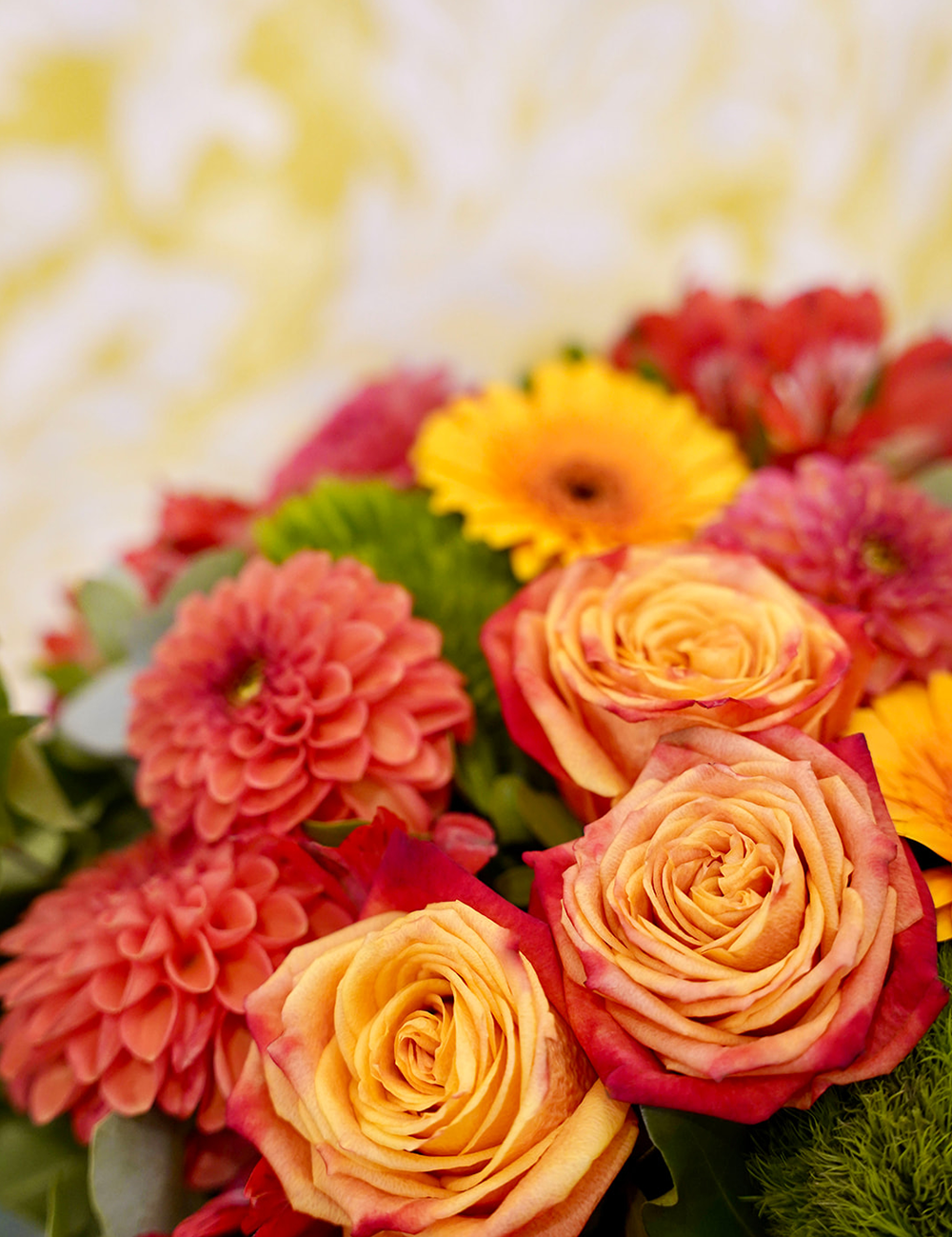 Zoom sur un bouquet de fleurs rond dans les tons rouges et oranges avec des touches de vert.