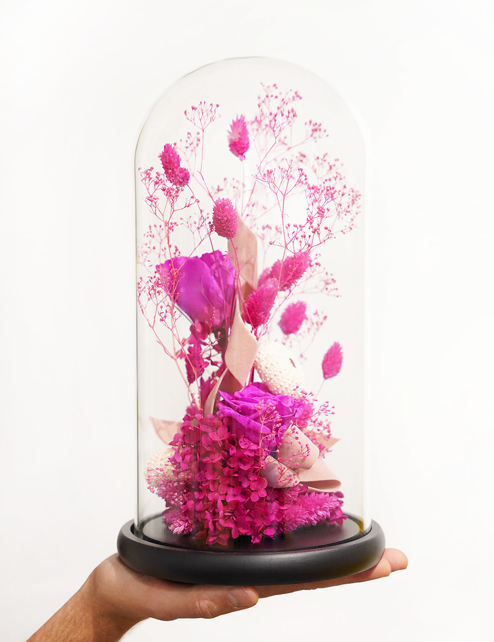 Composition de fleurs séchées sous cloche aux tons roses.